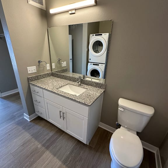 A bathroom with a white toilet and a washer and dryer stacked on top of each other.