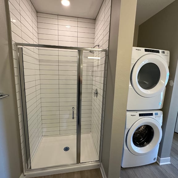 A white tiled shower area with a glass door and a washer and dryer at The Fitzroy Apartments in Birmingham, AL