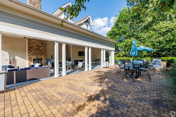 A patio with a table and chairs is surrounded by a brick floor and a white house.
