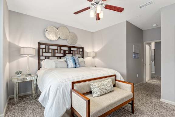 A bedroom with a bed, a bench, and a ceiling fan.