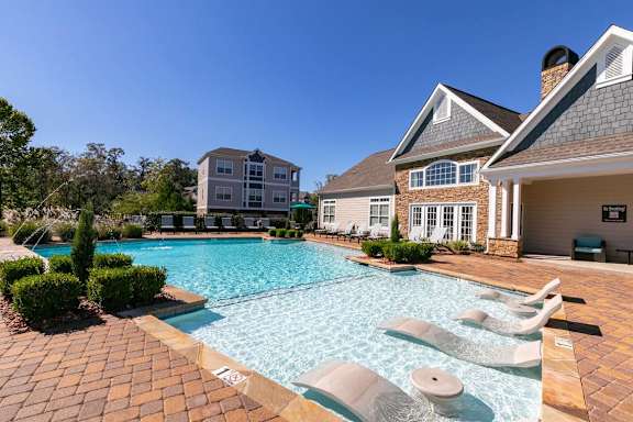 A swimming pool surrounded by a brick patio and lounge chairs.