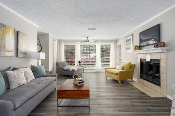 A living room with floor-to-ceiling windows, wood-look flooring, a ceiling fan, and a fireplace at Summerchase at Riverchase in Hoover, Alabama.