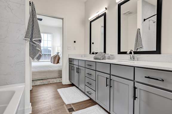 A bathroom with a white tub/shower combo, double vanity, and framed mirrors at West Row Townhomes and at West Row Townhomes at West Row Lofts and Townhomes in Birmingham, AL
