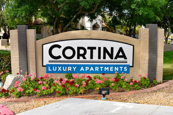 Signage reading Cortina Luxury Apartments with orange and red flowers planted in garden in front of sign
