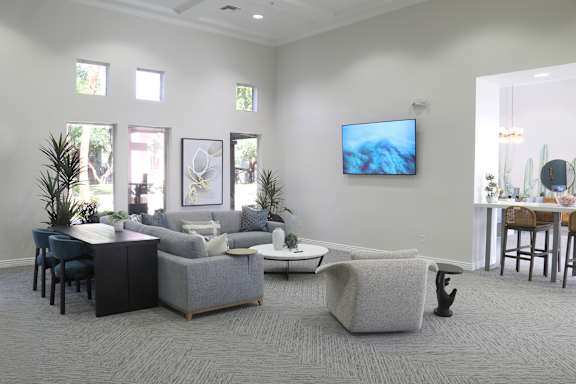 A living room with a grey sofa, a black cabinet, a white coffee table, and a television mounted on the wall.