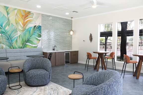 A room with a mural of leaves on the wall and grey chairs and tables.