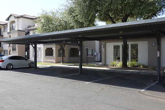 A white car is parked under a covered parking structure.