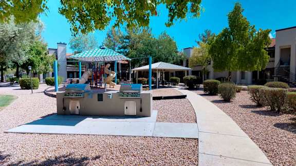 Two stainless steel gas BBQ grills located in in common area in front of shaded playground and covered gazebo