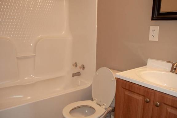 A white toilet with the seat up is in a bathroom with a white tub and sink.