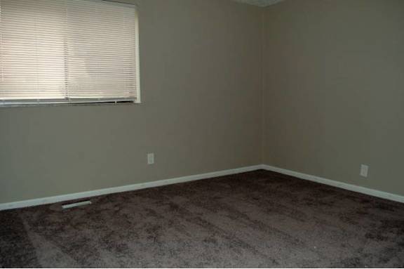 A room with a carpeted floor and a window with blinds.