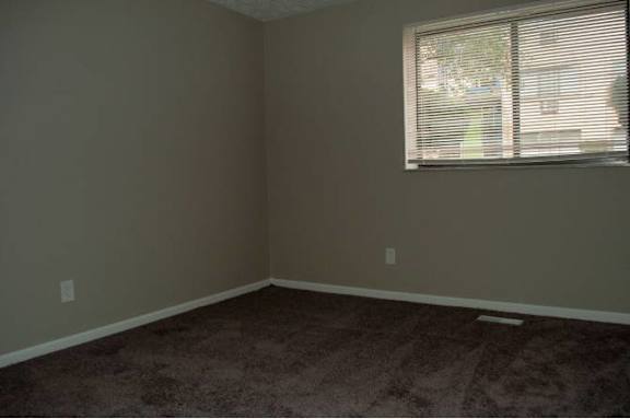 A room with a carpeted floor and a window with blinds.