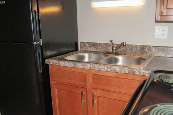 A black refrigerator sits next to a kitchen sink with a granite countertop.