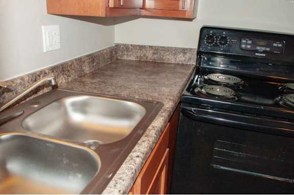 A black stove top oven sits next to a stainless steel double sink in a kitchen.