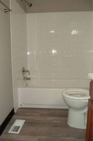 A white toilet in a bathroom with a white tub and tiled walls.