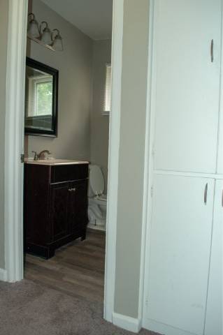 A white door is open to a bathroom with a white sink and a brown cabinet.