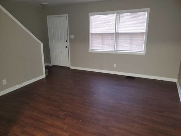 A room with a wooden floor and a window with blinds.