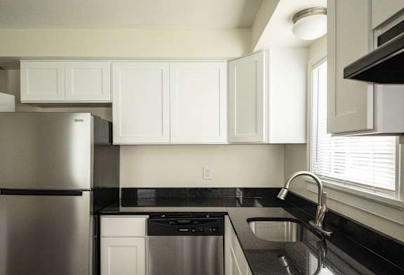 A kitchen with a stainless steel refrigerator and black countertops.
