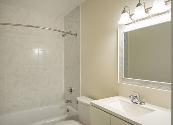 A white bathroom with a tub, sink, mirror and lights.
