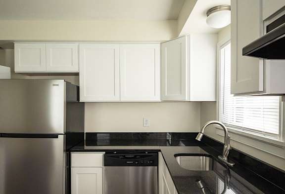 A kitchen with a stainless steel refrigerator and black countertops.