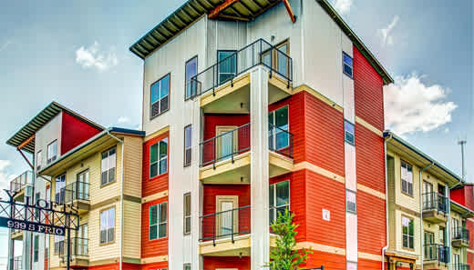A multi-story building with a red and beige exterior and a balcony on the second floor.
