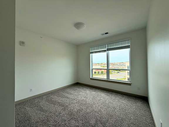 A room with a carpeted floor and a window overlooking a parking lot.
