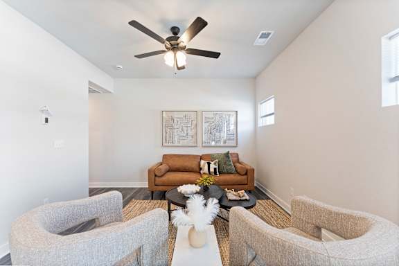 A living room with a brown couch, grey chairs, and a ceiling fan.