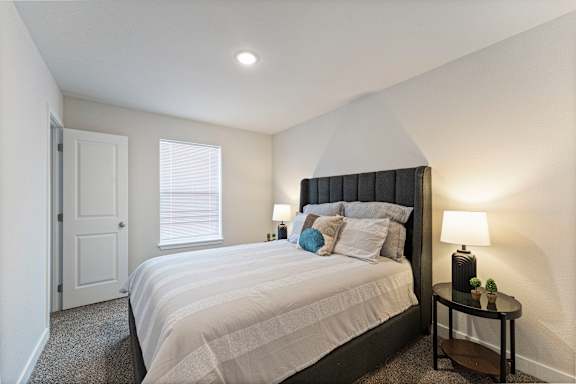 A bedroom with a large bed and a small table with a lamp.