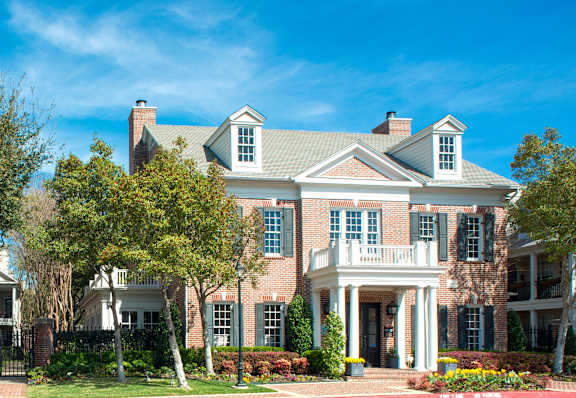 the front of a brick house with trees and a blue sky