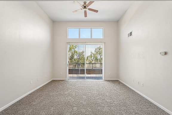 A spacious room with a ceiling fan and a sliding glass door leading to a balcony.