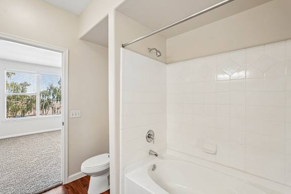 A white bathroom with a tub, toilet and window.