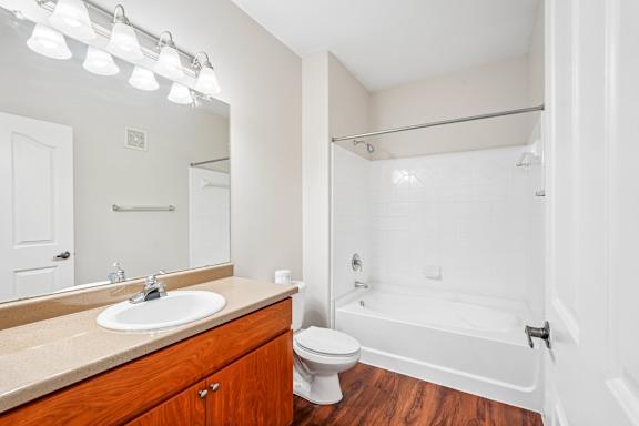 A white bathroom with a wooden vanity and a white bathtub.