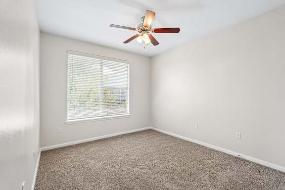 A room with a ceiling fan and a window with blinds.