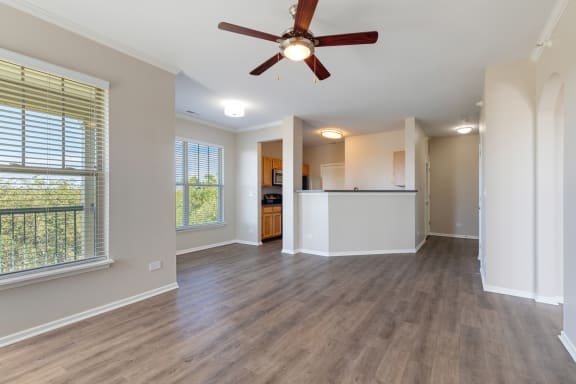 an empty living room with a ceiling fan and a kitchen