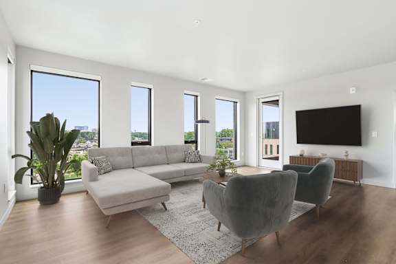 A living room with a grey couch, a grey chair, a grey ottoman, a television, and a potted plant.