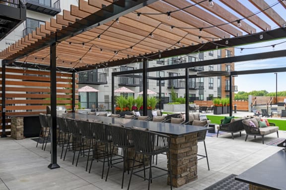 a patio with a long bar and chairs under a wooden roof