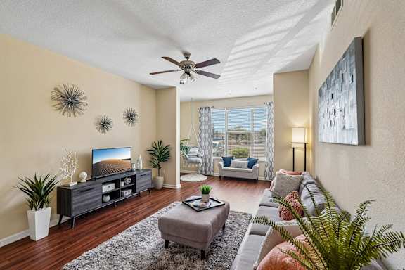 A living room with a grey sofa, a grey coffee table, a black cabinet, a ceiling fan, and a painting on the wall.