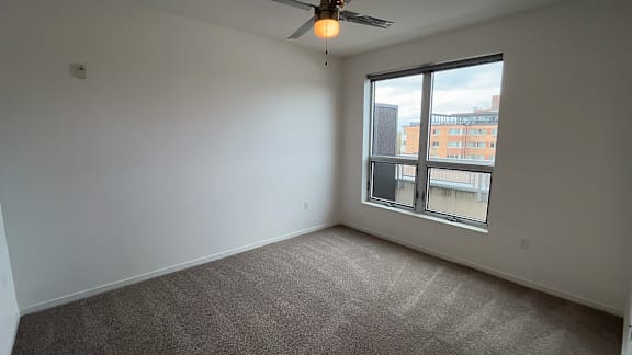 A room with a ceiling fan and a large window overlooking a city.