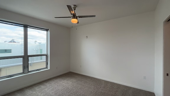 A room with a ceiling fan and a large window overlooking a cityscape.