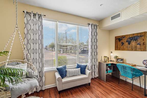 A room with a hanging chair and a couch with a window behind it.