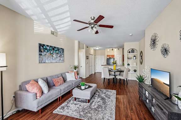 A living room with a grey couch, a coffee table, a television, and a ceiling fan.