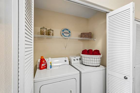 A laundry room with a washer and dryer, a basket of red balls, and a shelf with jars and a sign that says " Laundry".