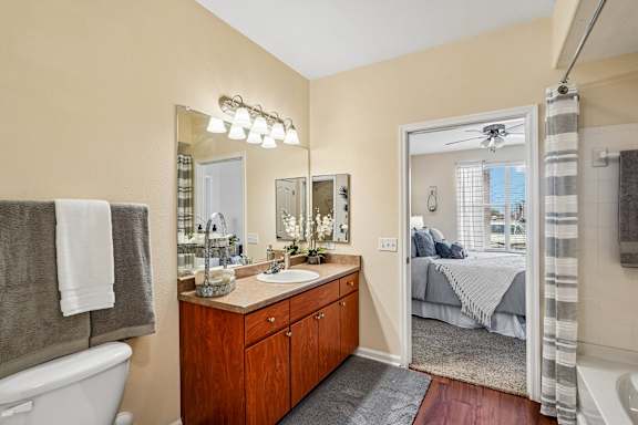 A bathroom with a white tub, a wooden vanity, and a bedroom in the background.