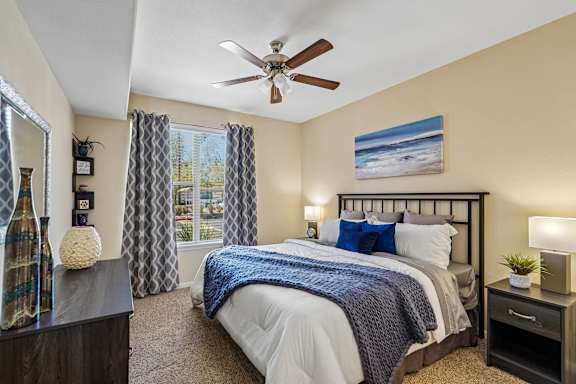 A bedroom with a large bed, a ceiling fan, and a painting on the wall.