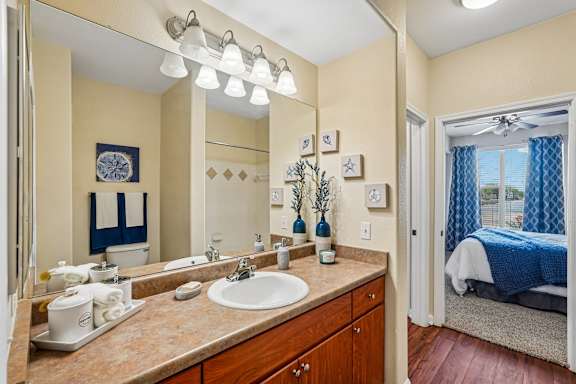A bathroom with a sink, mirror, and a bed in the background.