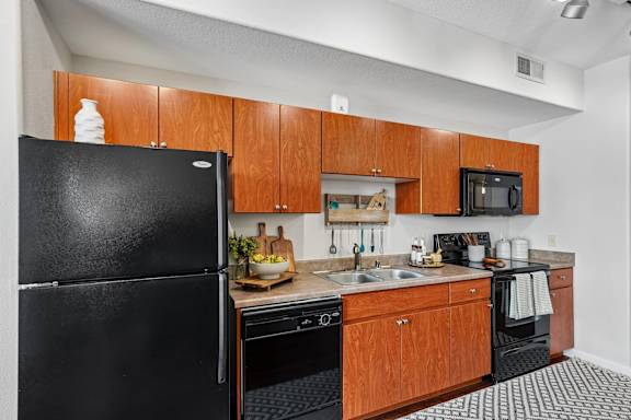 A black refrigerator stands next to a kitchen counter with a sink and a microwave.