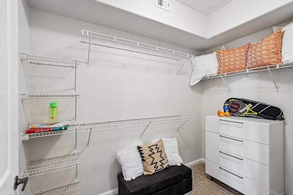 A white closet with a bench and a white dresser.