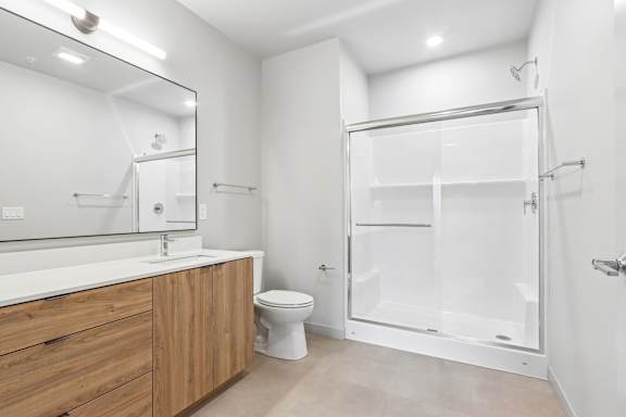 A white bathroom with a wooden vanity and a walk-in shower.