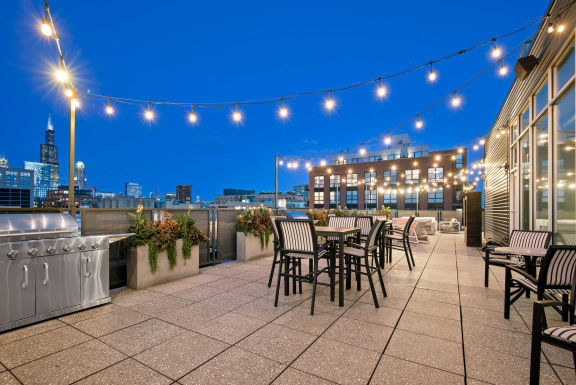 a rooftop terrace with tables and chairs and a view of the city at night