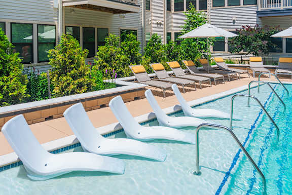A pool with white chairs and a building in the background.
