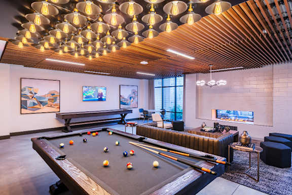 A pool table is in the middle of a room with a wooden ceiling and a bench.